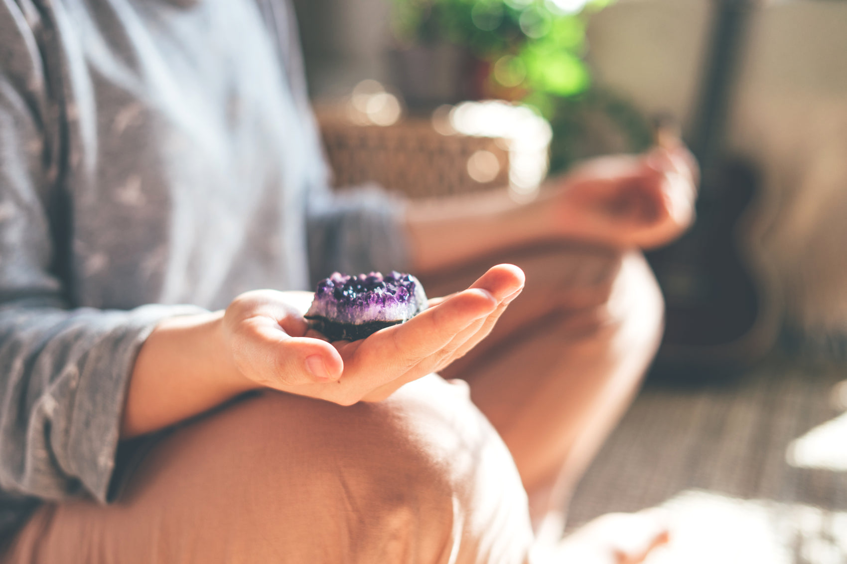 A person meditating while holding an amethyst crystal geode, with a soft background.