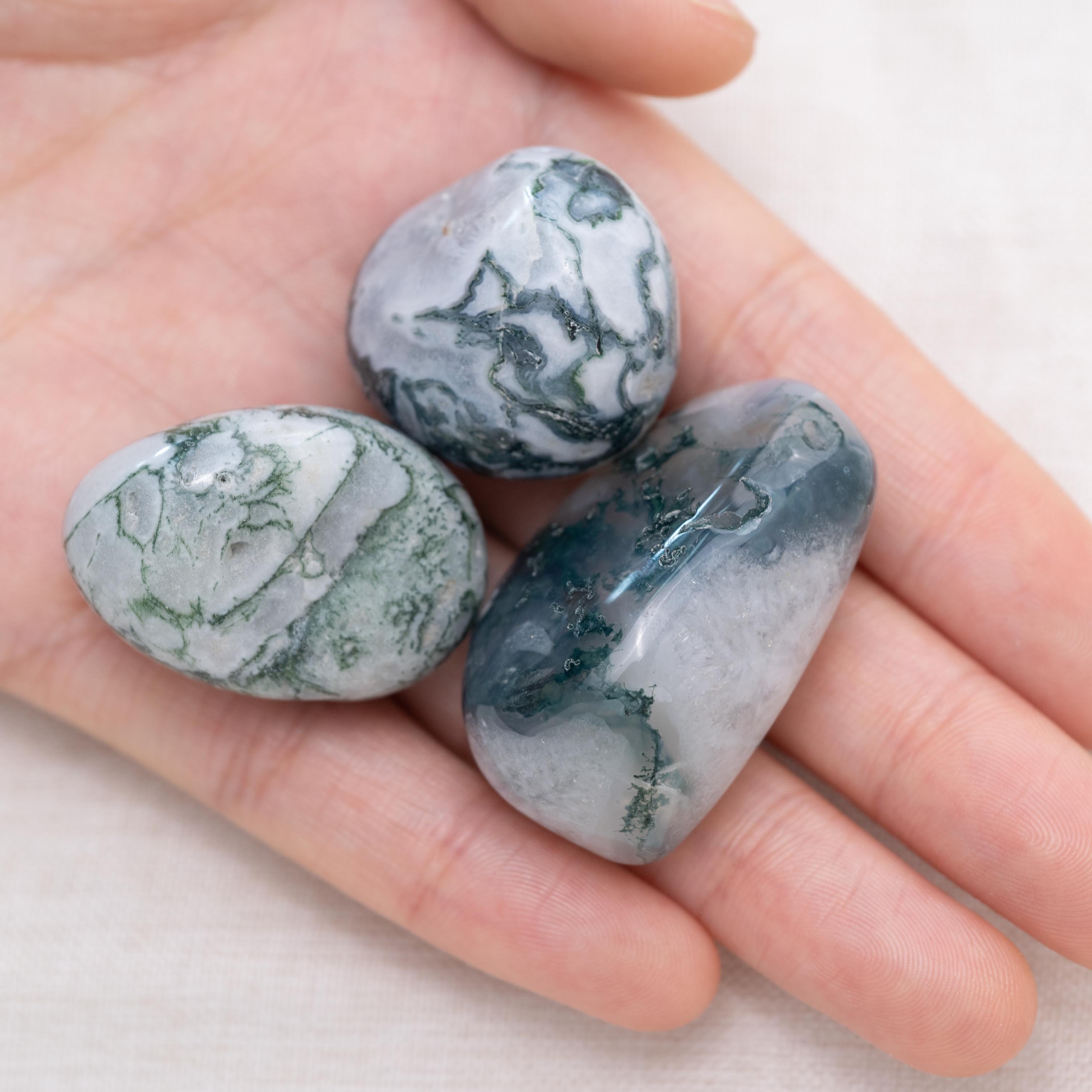 Hand holding Moss Agate tumbled stone for growth and stability