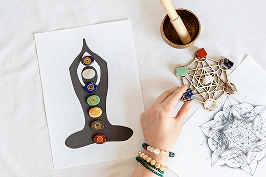 Seven chakra stones aligned on a yoga pose silhouette, each representing a different chakra.