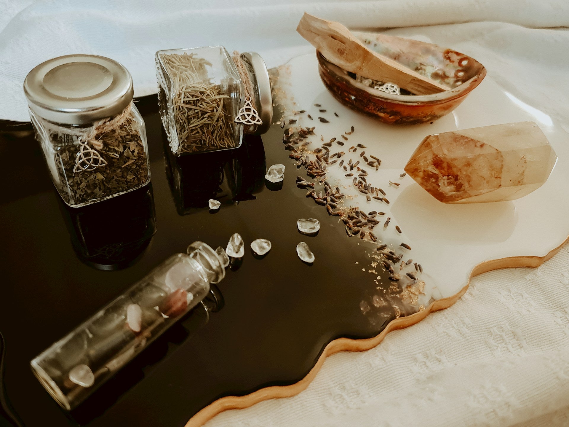 Healing setup with crystals, dried herbs in glass jars, and gemstones arranged on a black and white tray.