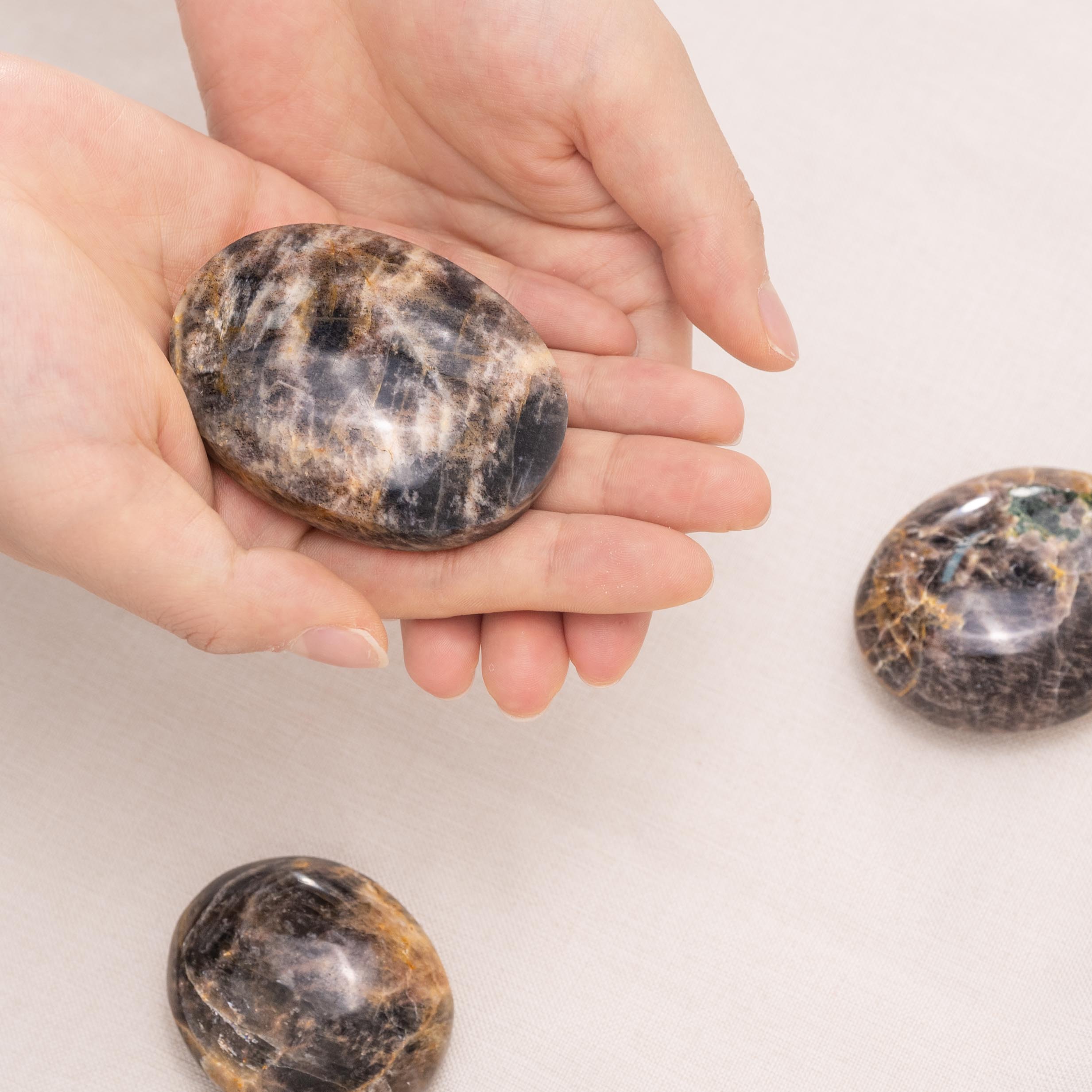 Hand-held Black Moonstone Palmstone with smooth surface showing natural grey sheen, ideal for meditation and spiritual healing