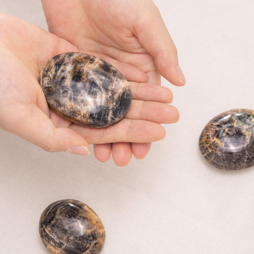 Hand-held Black Moonstone Palmstone with smooth surface showing natural grey sheen, ideal for meditation and spiritual healing