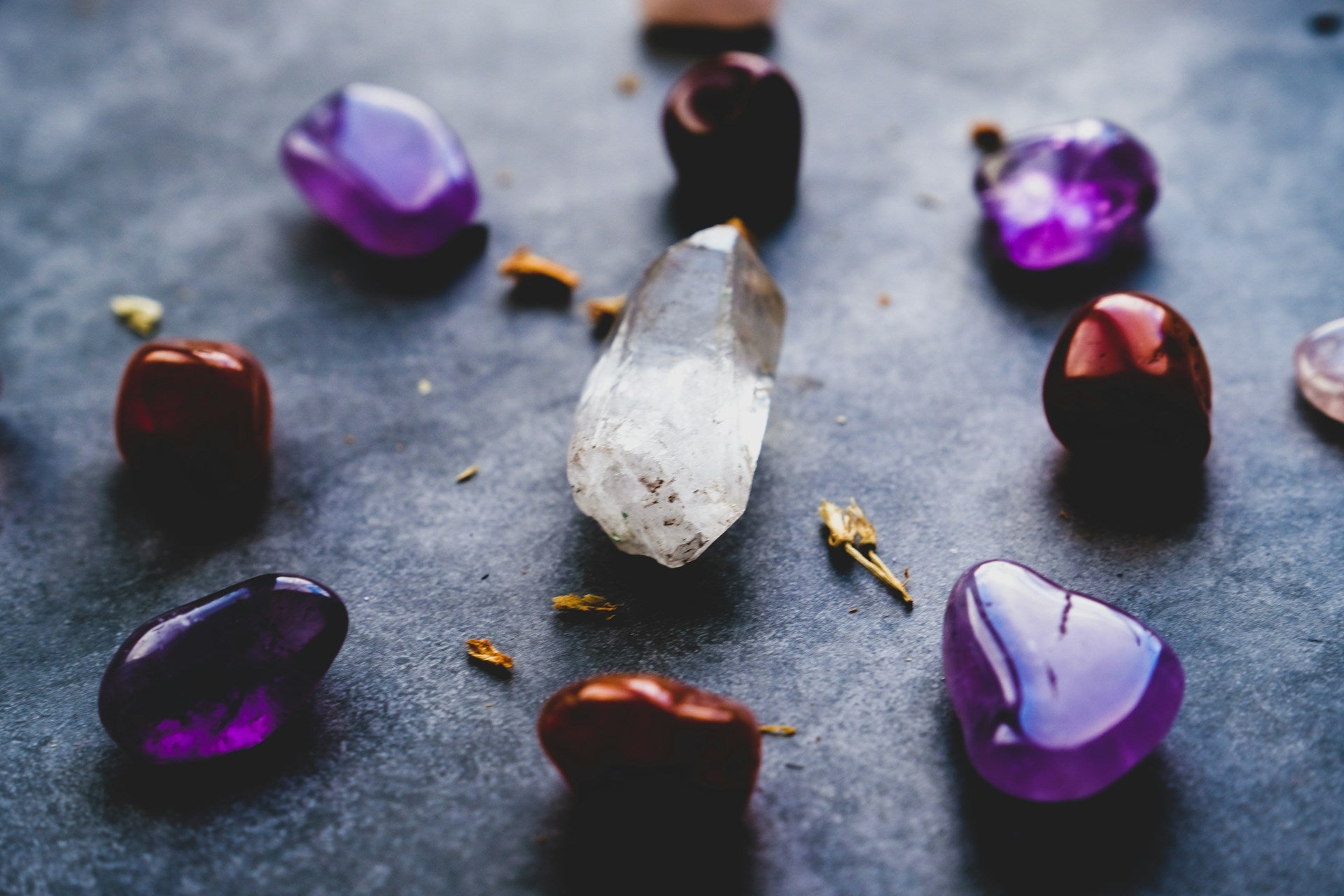 A clear quartz point surrounded by various tumbled crystals, including amethyst and carnelian, on a dark surface.