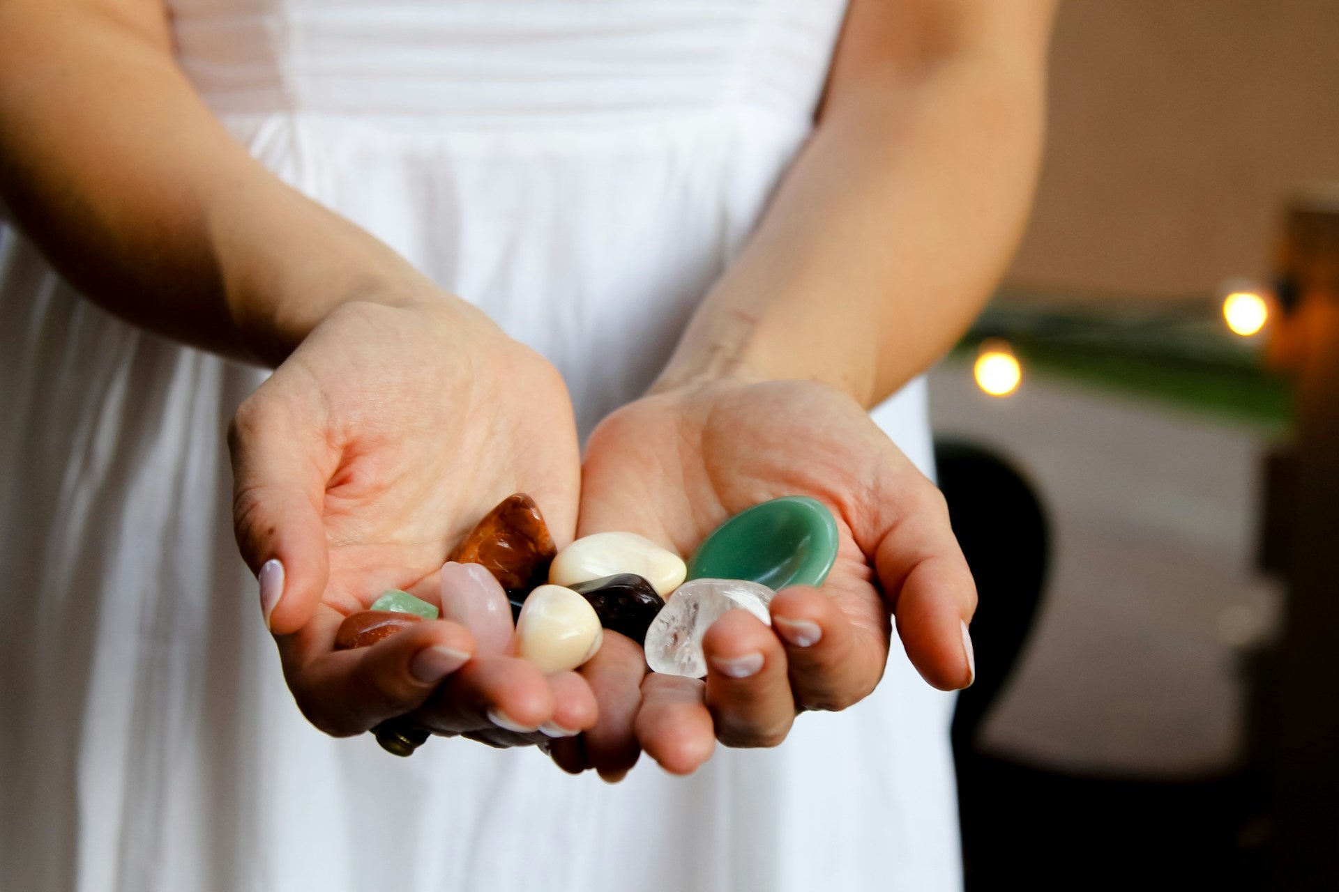 Close-up of hands holding various tumbled healing crystals, with a soft background.